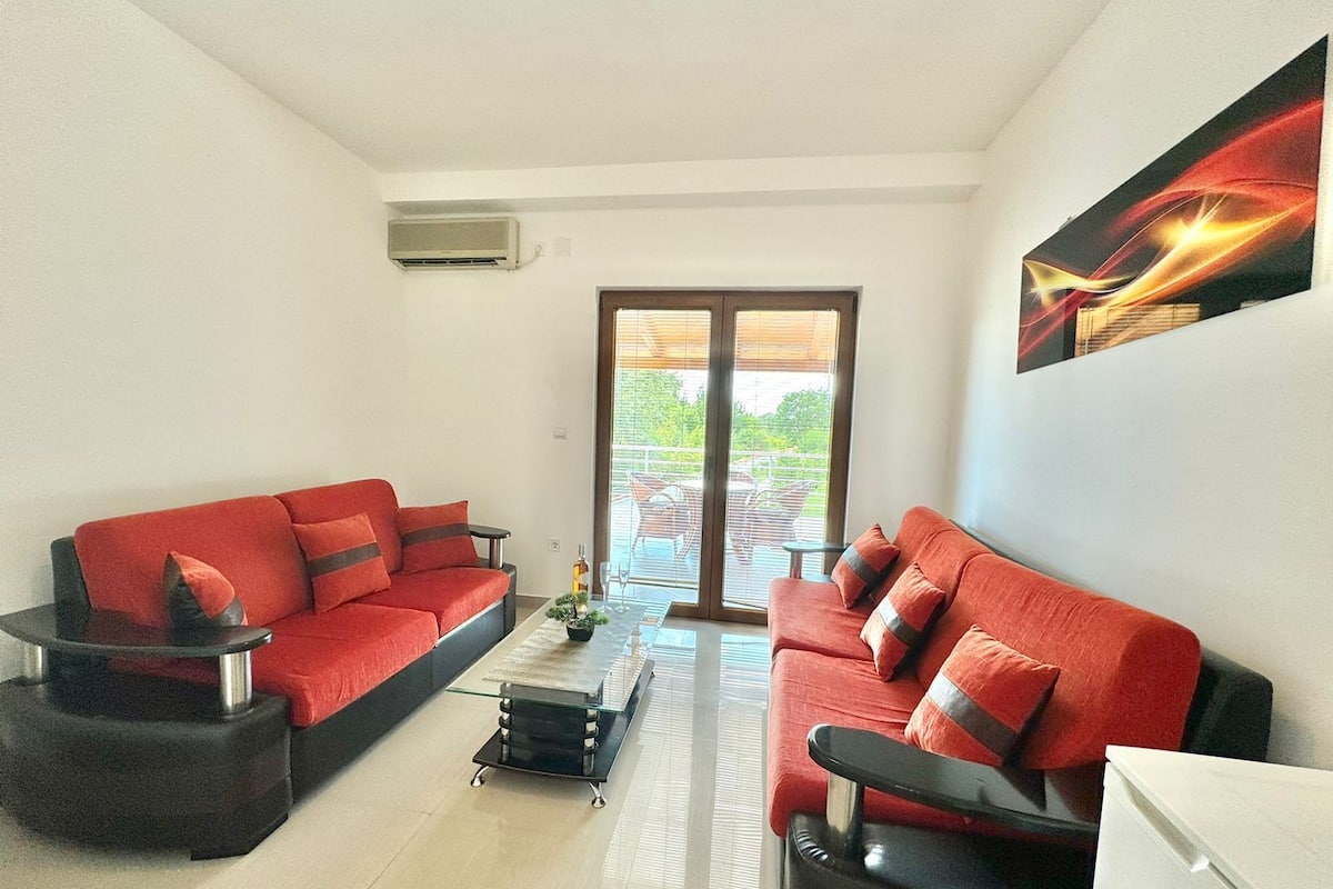 A modern living room with two red sofas, a glass coffee table, and a view of the outdoors through a sliding glass door.