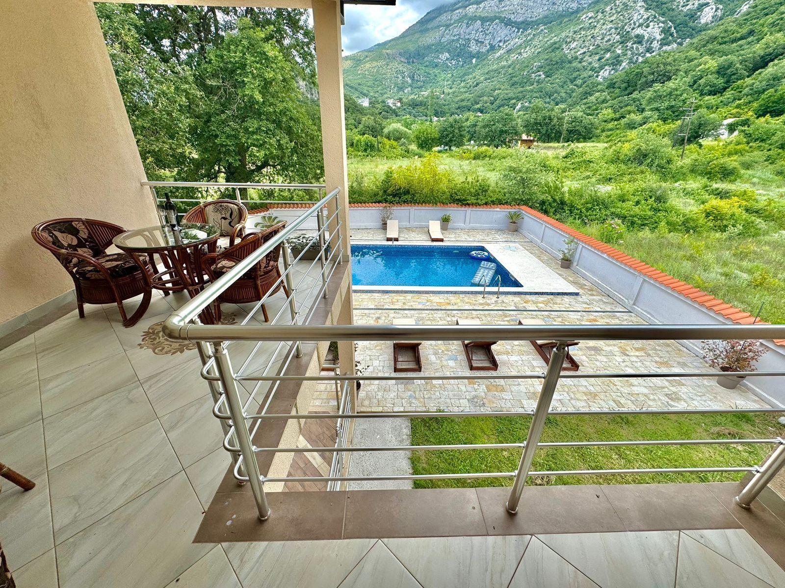 A balcony with a pool, wicker furniture, and a view of a mountainous landscape.