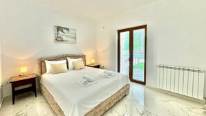 A bedroom with a large bed, two bedside tables with lamps, a painting on the wall, and a window with blinds. - Stars Residence (Petrovac)