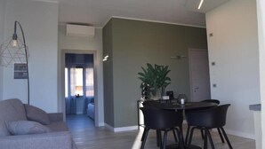 Een moderne woonkamer met een grijze bank, een eettafel met vier stoelen en een potplant.