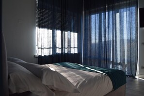 Une chambre à coucher avec un lit, une fenêtre ornée de rideaux légers et une vue sur l’extérieur.