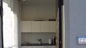 Un couloir étroit mène à une cuisine dotée de meubles blancs, d’un plan de travail et d’un évier.
