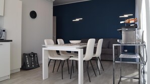 Une cuisine moderne avec une table et des chaises blanches, un mur d’accent bleu foncé et une machine à café.