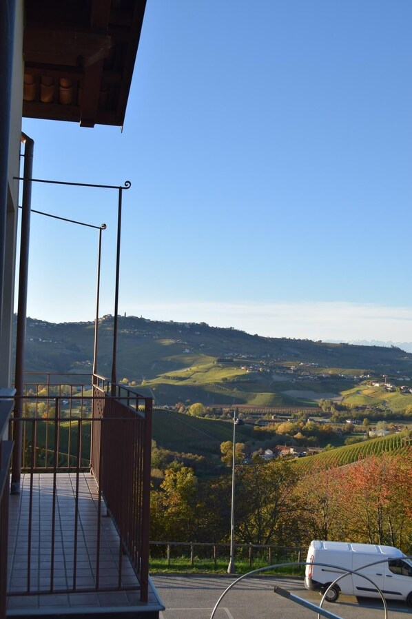 Un balcon donnant sur un paysage vallonné, un fourgon blanc garé au premier plan et un ciel bleu dégagé.