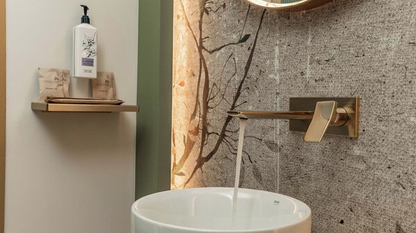 A bathroom with a white sink, a wall-mounted faucet, and a shelf with toiletries. - MiraVita Hotel - Adults Only (Chania)
