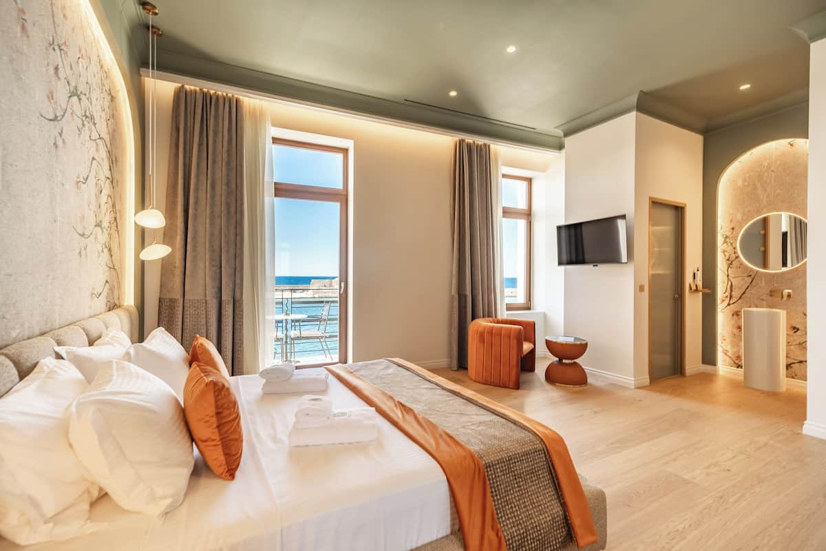 A hotel room with a large bed, a TV, a balcony with a view, and a bathroom with a mirror.