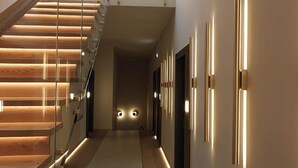 Un intérieur moderne avec un escalier en bois, une rampe en verre et des luminaires fixés au mur.
