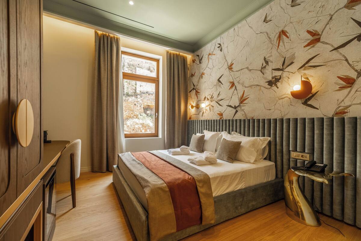 A modern bedroom with a large bed, a bedside table with a lamp, and a window with curtains.