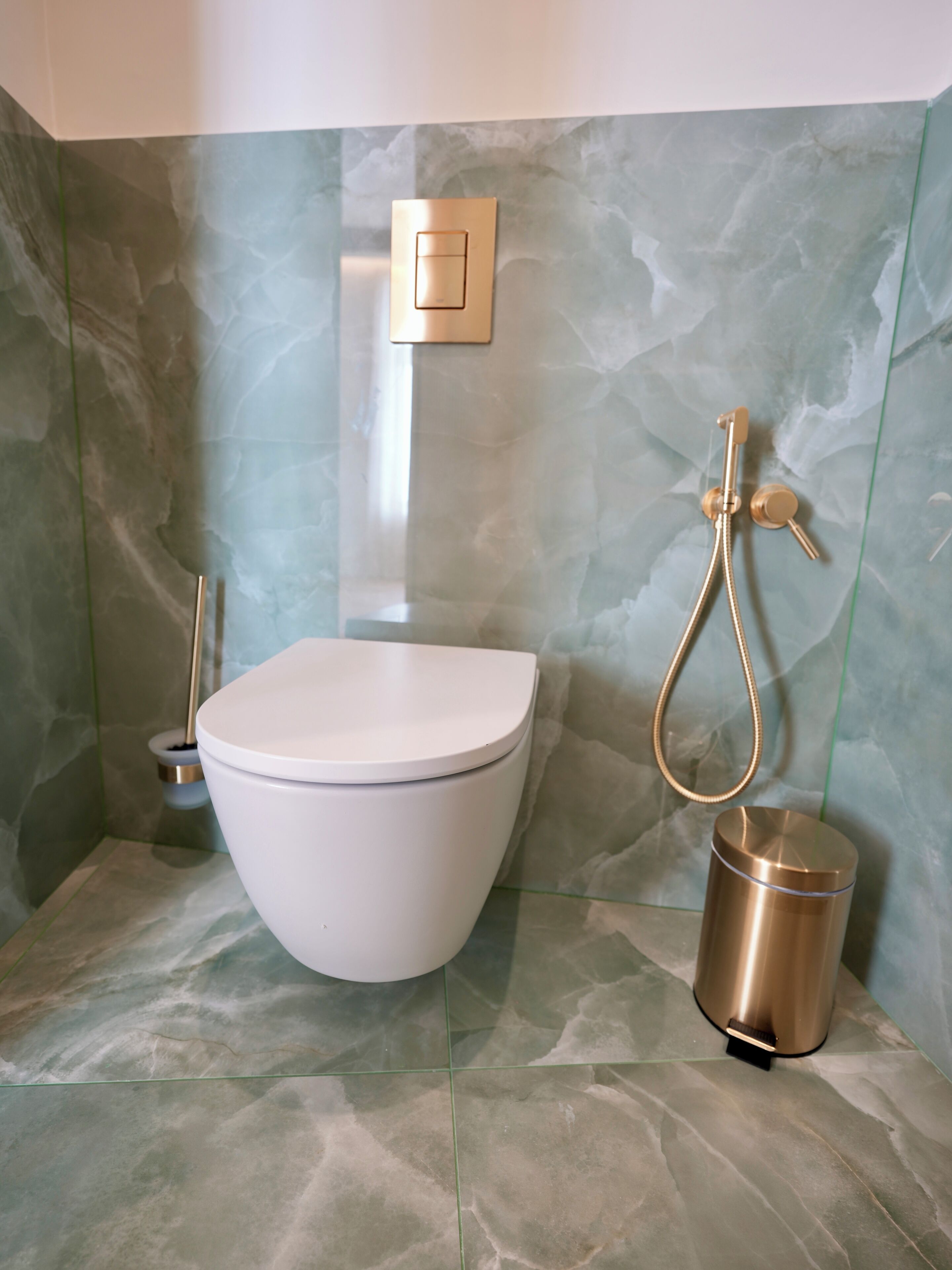 A bathroom with a white toilet, a gold showerhead, and a gold bucket.