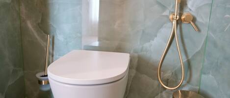 A bathroom with a white toilet, a gold showerhead, and a gold bucket.
