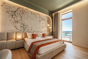 A modern hotel room with a large bed, a sofa, a wall mural, and a balcony with a view of the sea. - MiraVita Hotel - Adults Only (Chania)
