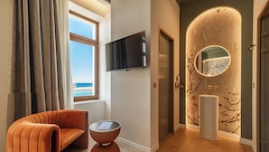 Une pièce moderne avec un canapé aux lignes courbes, une table ronde, un téléviseur à écran plat et un miroir original fixé au mur.