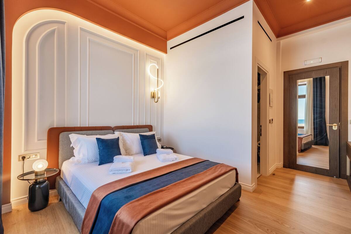 A hotel room with a large bed, a bedside table with a lamp, and a view of the hallway.