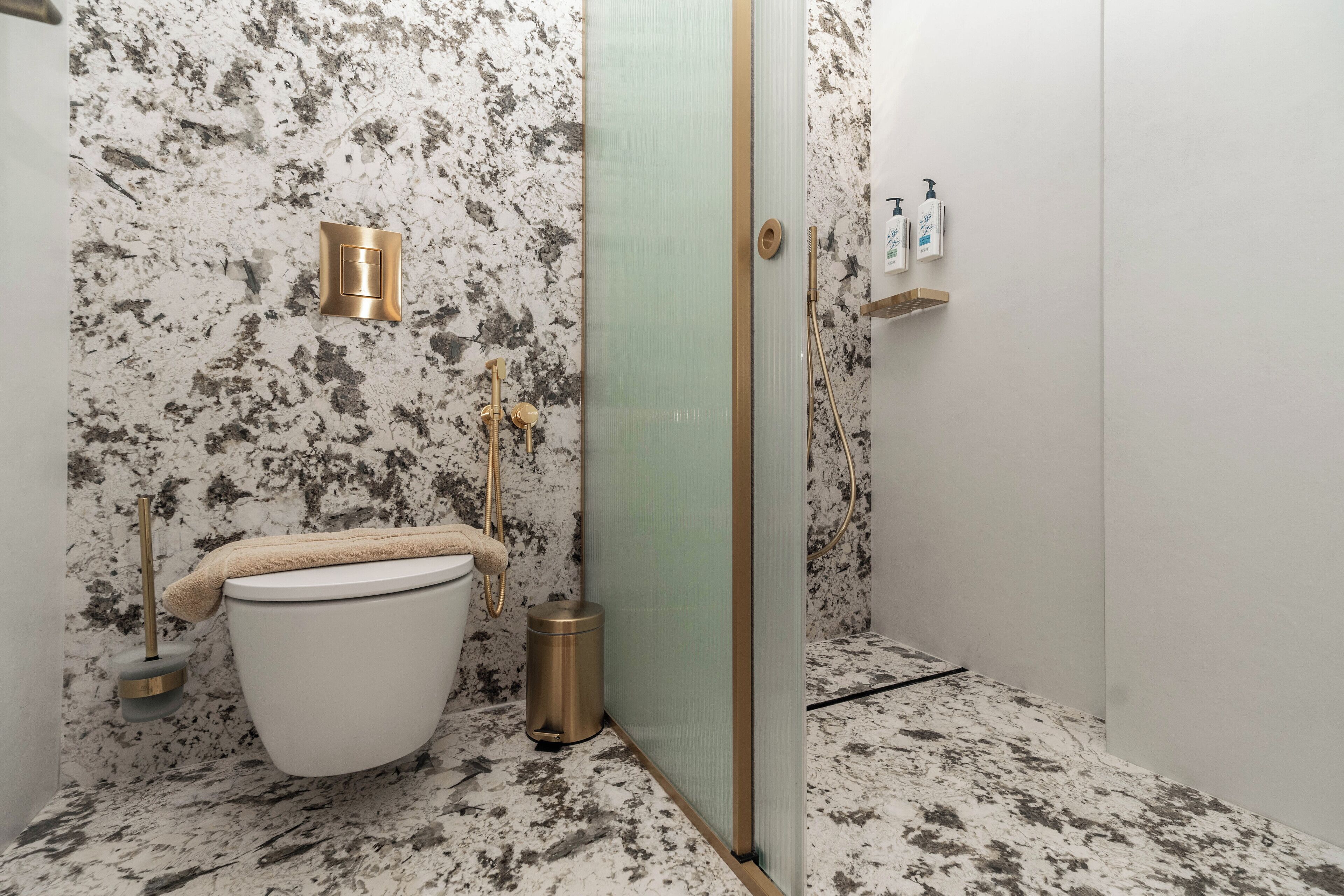 Een badkamer met een marmeren vloer, toilet, douchecabine en een handdoekhouder.