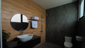 A modern bathroom with a round mirror, a white sink, a towel rack, a shower, and a toilet. - LuckyStar Hotel (Pleiku)