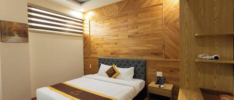 Una cama bien hecha con cabecera, una mesita de noche con teléfono y paneles de madera en la pared.