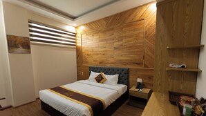 A hotel room with a wooden headboard, a neatly made bed with a white and brown bedspread, a bedside table with a lamp, and a small shelf with toiletries. - LuckyStar Hotel (Pleiku)