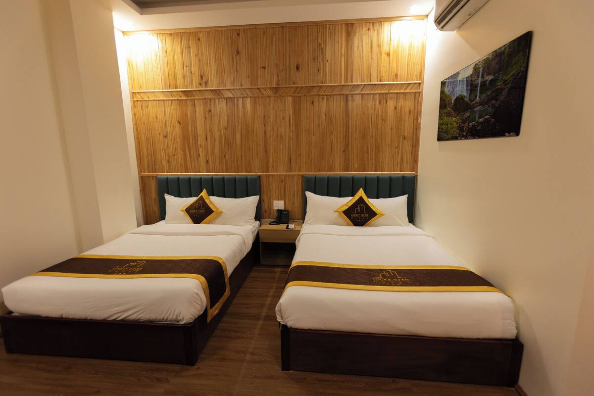 A hotel room with two beds, wooden paneling on the wall, a nightstand, and a painting.