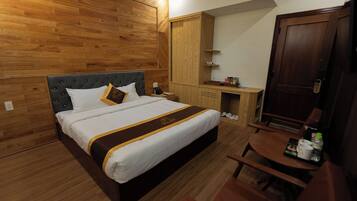 Habitación de hotel con una cama grande, paneles de madera, un armario de madera, una mesita pequeña con una bandeja y una puerta con picaporte.