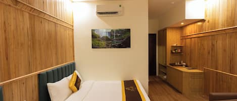 A hotel room with a bed, bedside table, phone, and a picture on the wall.