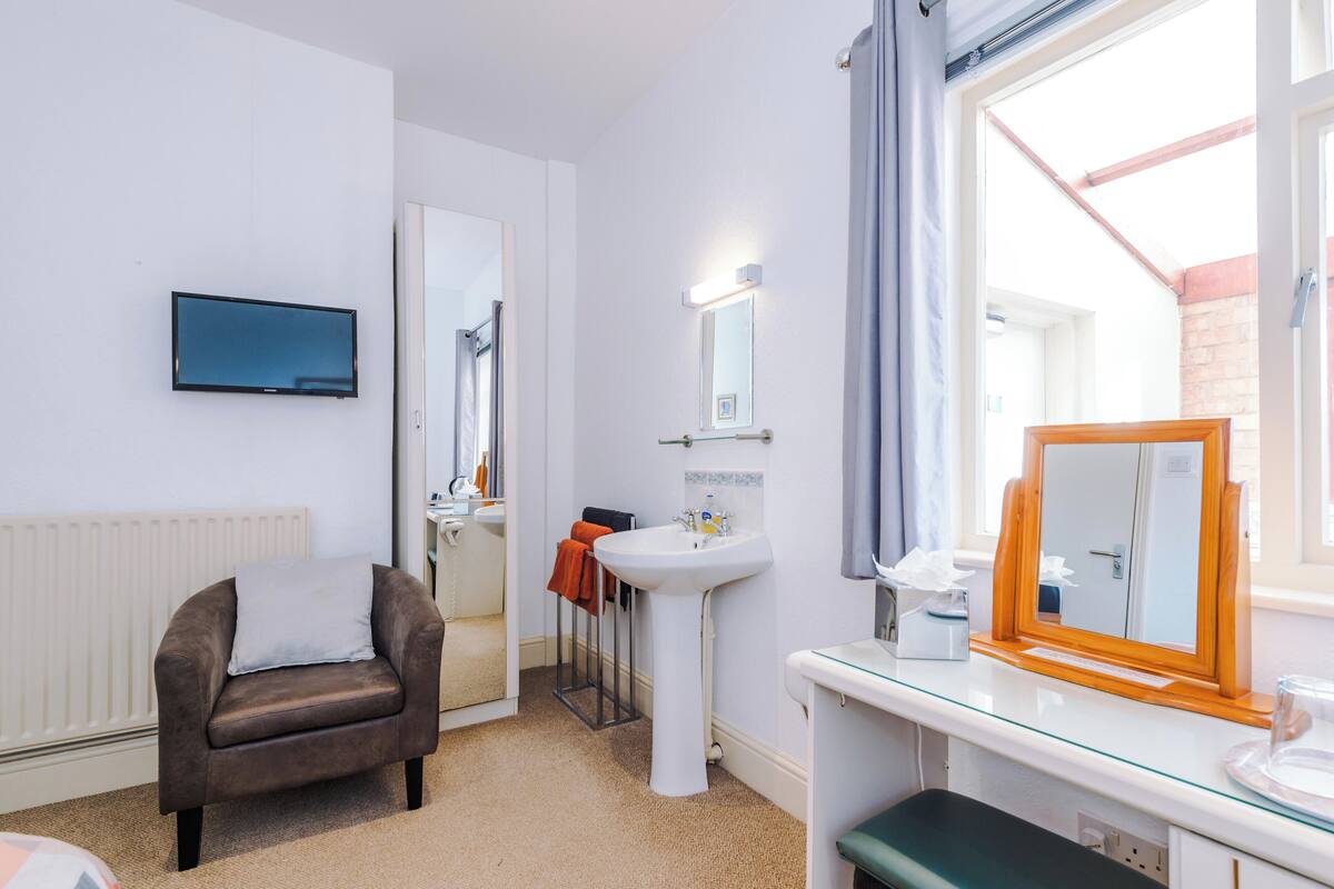 Un baño moderno con un lavamanos blanco, un espejo y un televisor montado en la pared.