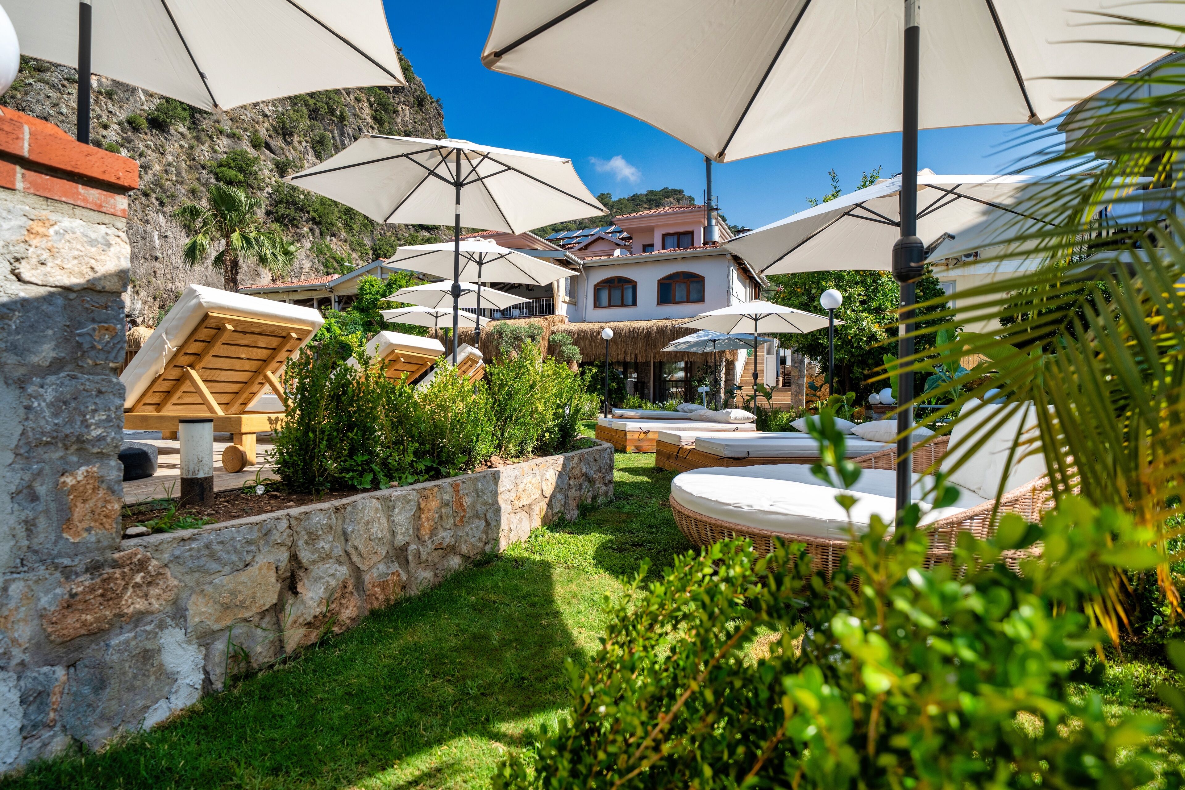 Un patio con mobiliario exterior y sombrillas, rodeado de muros de piedra y vegetación.
