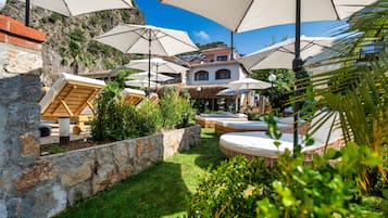 Un patio con mobiliario exterior y sombrillas, rodeado de muros de piedra y vegetación.
