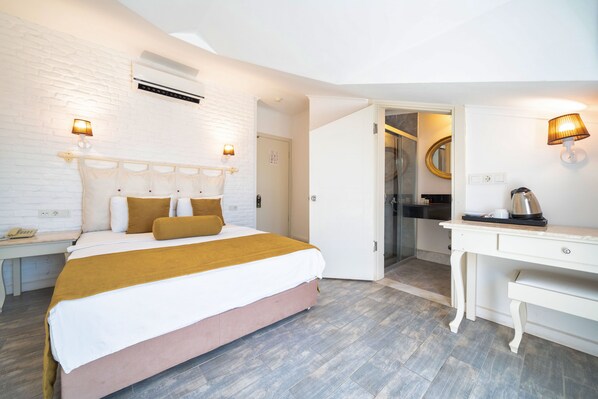 Habitación de hotel con cama, mesitas de noche, escritorio y baño visible a través de una puerta abierta.