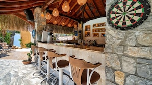 Un espace bar avec des murs en pierre, des tabourets de bar en bois et un jeu de fléchettes.