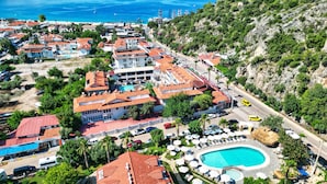 Une ville côtière qui abrite un hôtel imposant, composé de plusieurs bâtiments, doté d’une piscine et bordé d’une route où circulent des véhicules.