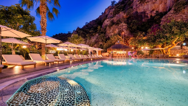Un espace piscine doté de chaises longues et de parasols, entouré d’un paysage montagneux.