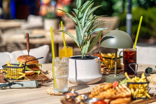 Une table à manger avec un hamburger, des frites, une boisson et une plante en pot.