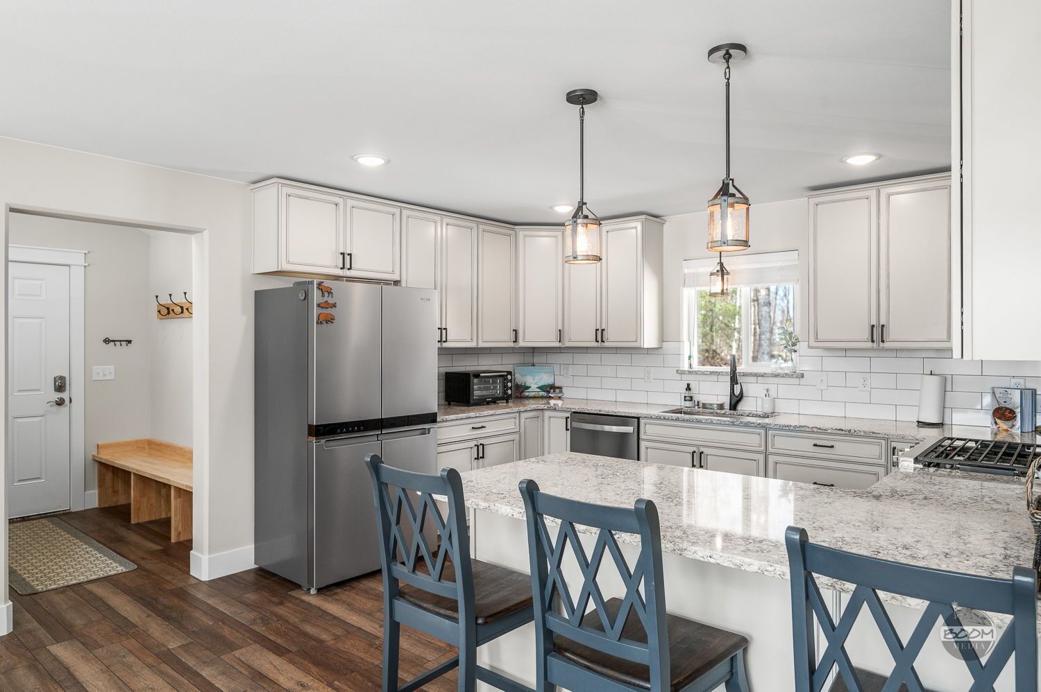 A modern kitchen with white cabinets, a stainless steel refrigerator, a built-in oven, a microwave, and a large island with bar stools.