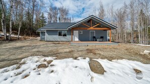 A modern two-story house with a covered porch and a garage, surrounded by a forested area.
