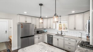 A modern kitchen with white cabinets, stainless steel appliances, granite countertops, and pendant lighting.