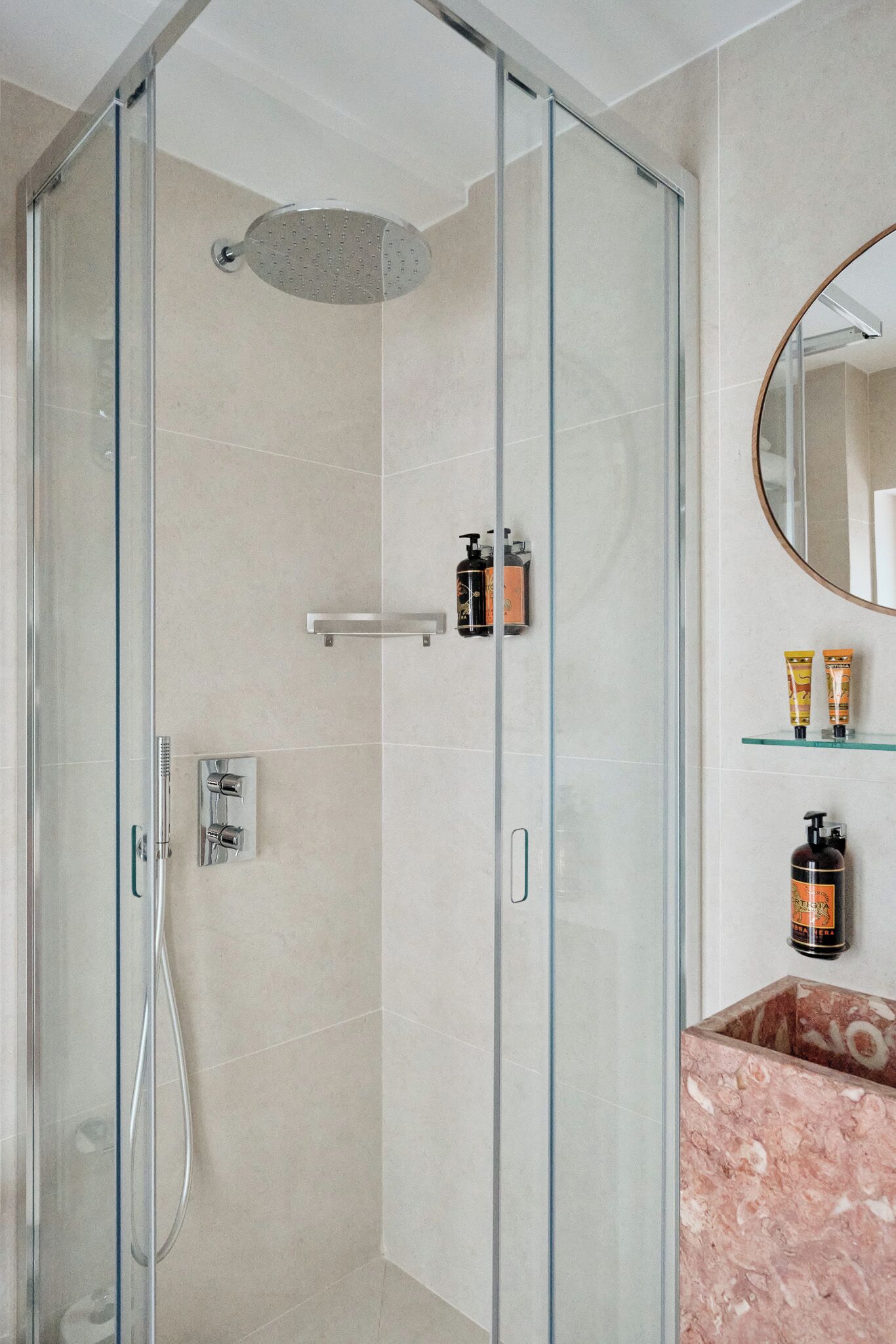 A modern bathroom with a glass-enclosed shower, a marble sink, and toiletries on a shelf.