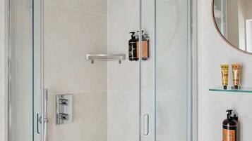 A modern bathroom with a glass-enclosed shower, a marble sink, and toiletries on a shelf.