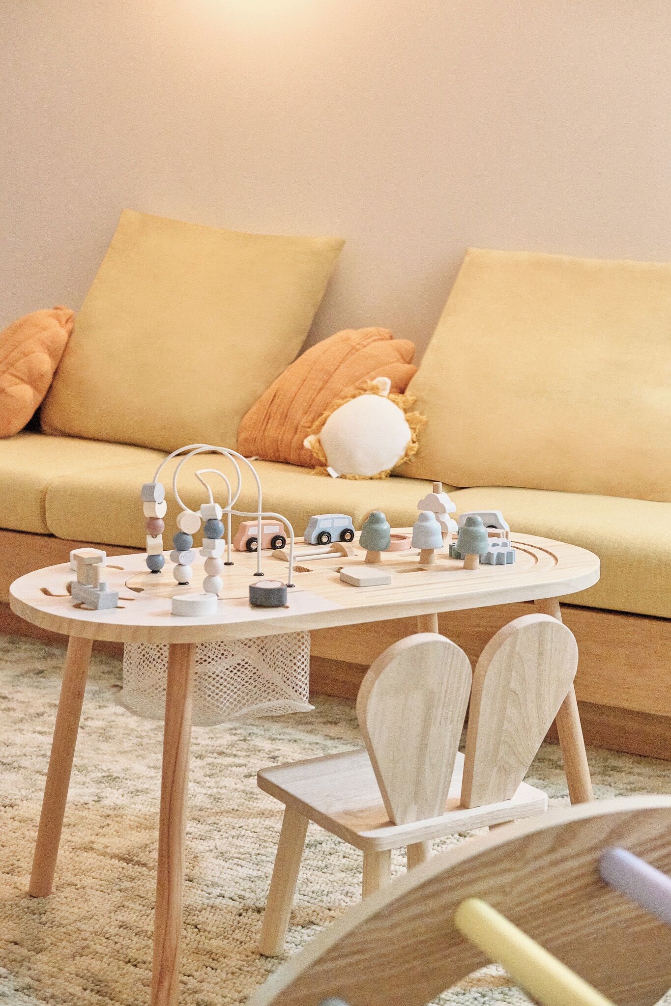 Ein Holztisch zum Spielen mit Spielzeug und einem kleinen Stuhl in einem gemütlichen Zimmer mit einer Couch und Kissen.