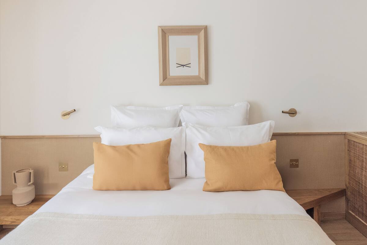 Habitación de hotel con cama, dos almohadas, mesita de noche y un reloj de pared.