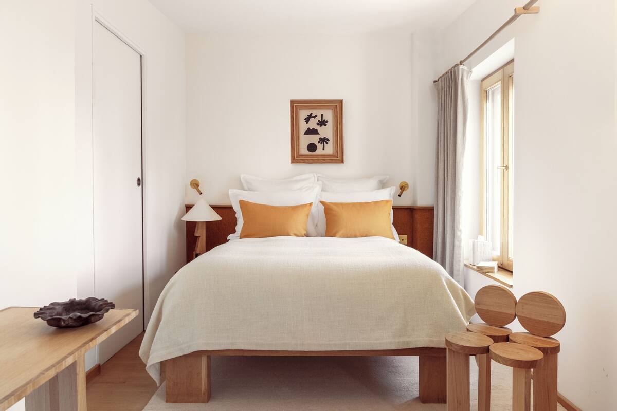 Un dormitorio ordenado con cama, mesitas de noche y una ventana con cortinas.