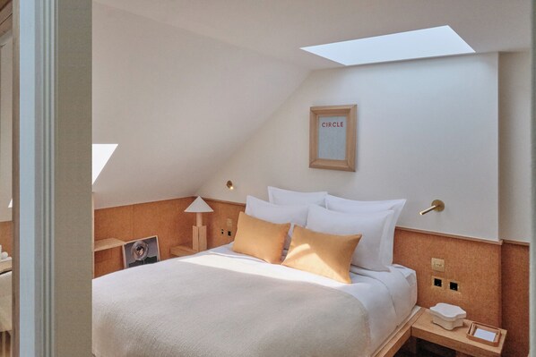 Une chambre d’hôtel moderne avec un lit soigneusement fait, une table de chevet avec une lampe et un tableau encadré au mur.