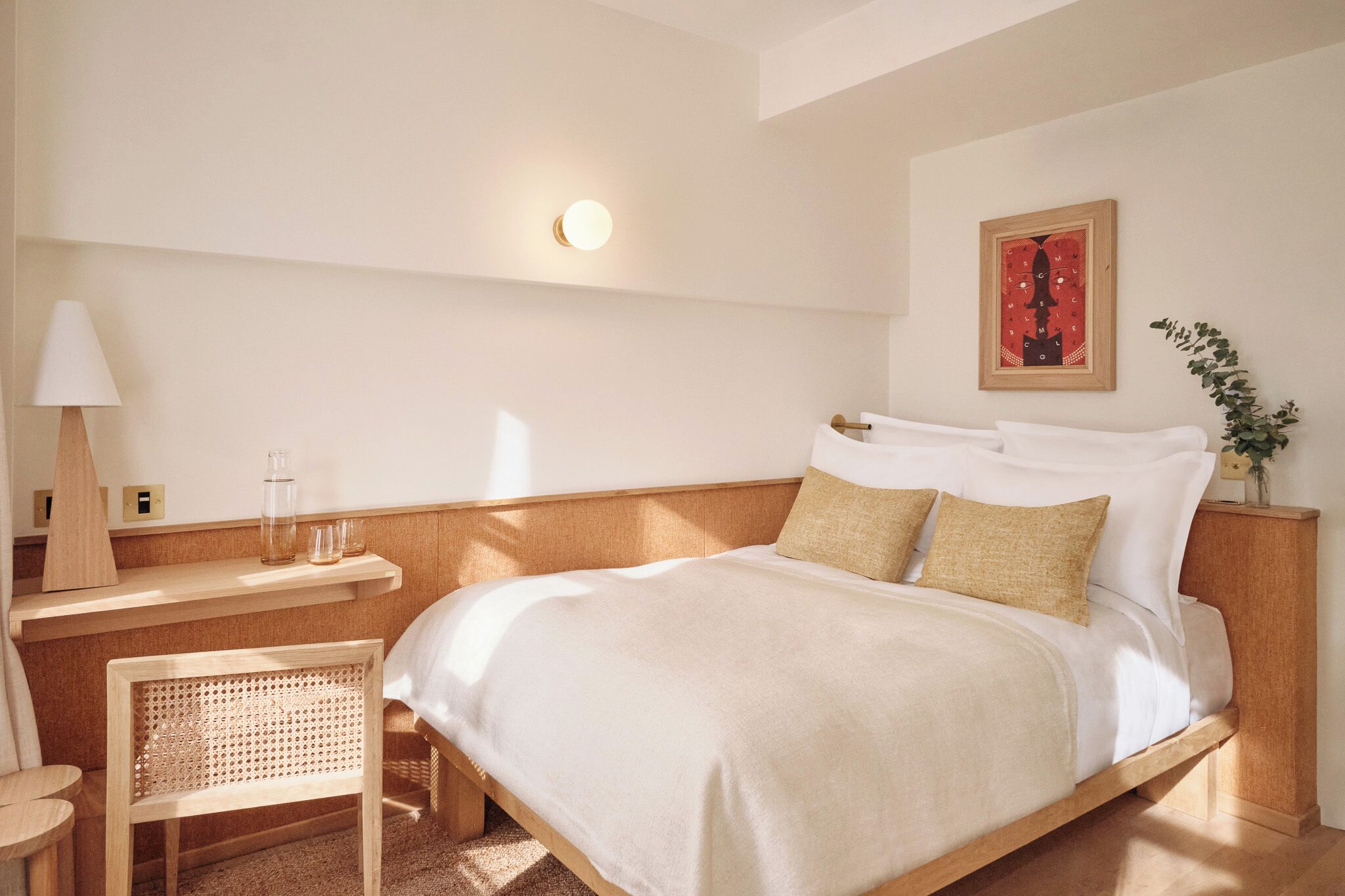 Une chambre d’hôtel bien rangée, avec un lit, une table de chevet, une lampe et une petite chaise.