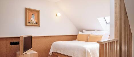A bedroom with a bed, a desk, a framed picture on the wall, a skylight, and a wooden slat railing.