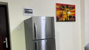 Un refrigerador de acero inoxidable en una cocina con piso de baldosas y una puerta a la izquierda.
