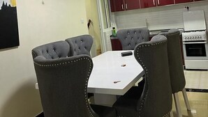 Un comedor con una mesa blanca y cuatro sillas grises tapizadas, una cocina roja con armarios blancos y un horno blanco.