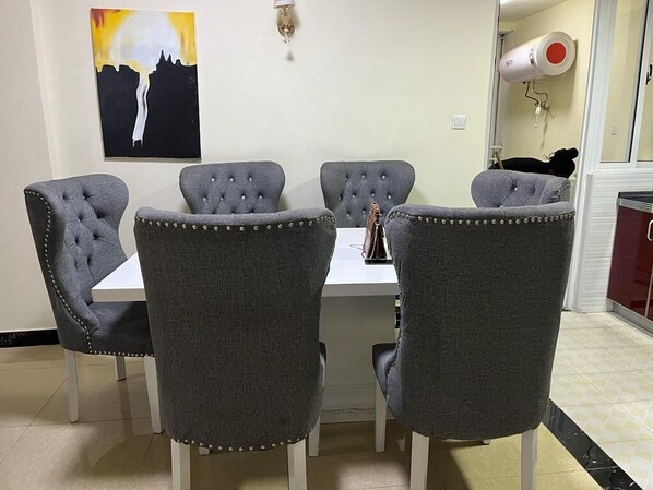 A dining area with a white table and grey upholstered chairs with button detailing.