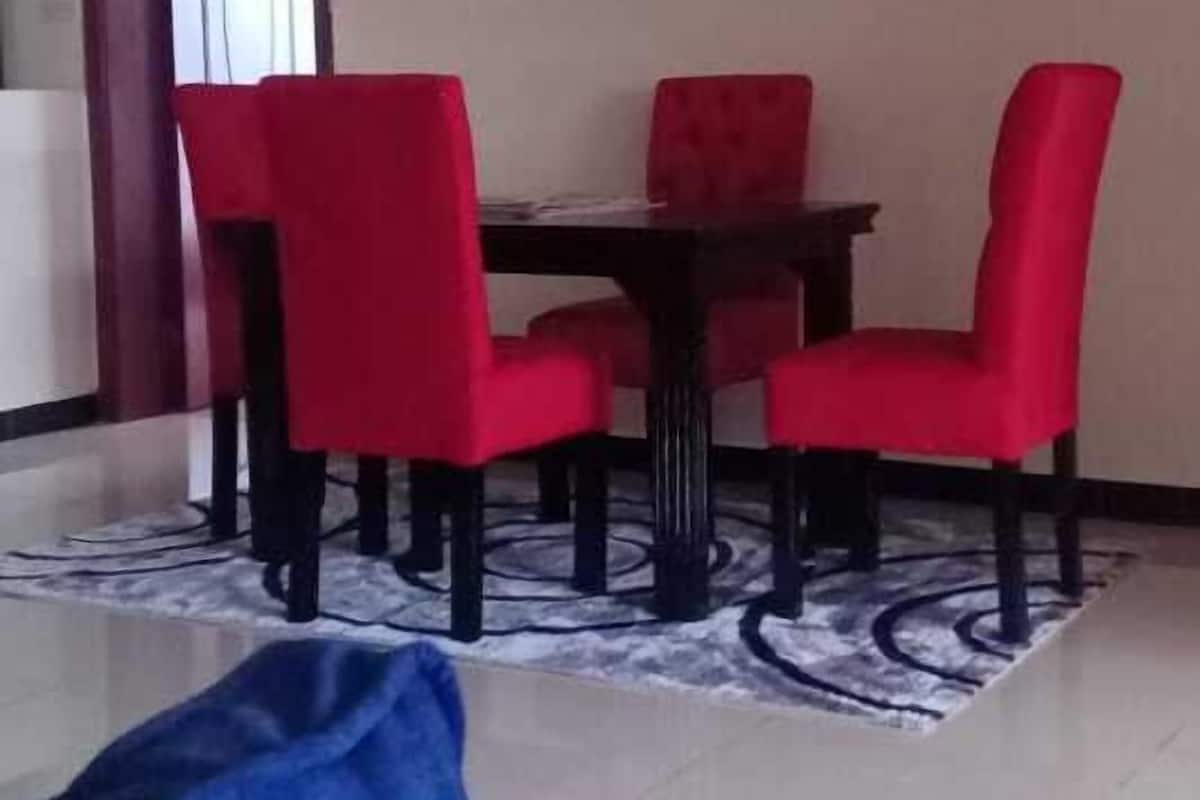 A dining area with a table and four red chairs, a blue sofa, and a patterned rug.