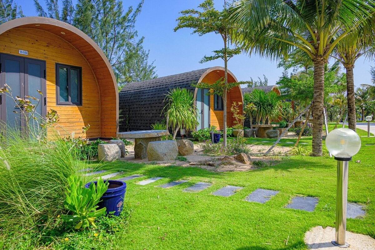 Une rangée de logements en forme de capsules, construits en bois, avec un chemin en pierre et une végétation luxuriante.