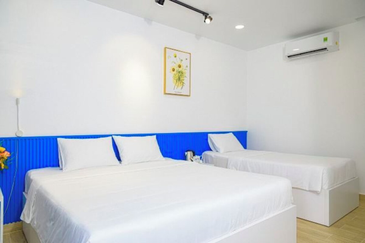 A hotel room with two beds, a blue headboard, white bedding, a wall-mounted air conditioner, and a framed picture on the wall.