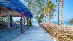 A covered walkway with a view of the sea, palm trees, and a beach.